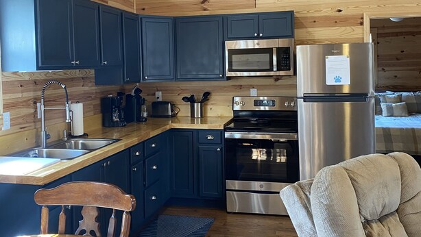 A modern kitchen with wooden ceiling, dark blue cabinets, stainless steel appliances, and a dining area with a wooden table and chairs.