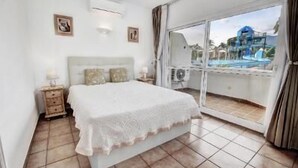 Un dormitorio con una cama grande, una mesita de noche, un equipo de aire acondicionado y vista a una piscina a través de una puerta de cristal.