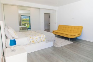 A bedroom with a bed, a yellow sofa, a white bedside table, and a mirror.
