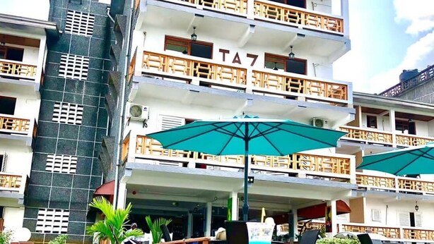 A multi-story hotel with balconies, a swimming pool with a pink float, and umbrellas.