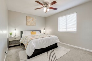 A bedroom with a bed, nightstands, a ceiling fan, a window with blinds, and a wall art piece. - Relax Poolside: Central Group Getaway in Mesa! (Mesa)