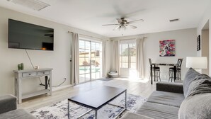 A modern living room with a flat-screen TV, grey sofa, coffee table, and a dining area with a table and chairs.