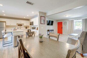 A modern kitchen with white cabinets, a dining area with a wooden table and chairs, and a living room with a grey sofa and a TV on the wall. - Relax Poolside: Central Group Getaway in Mesa! (Mesa)