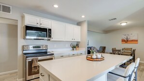 A modern kitchen with white cabinetry, stainless steel appliances, and a central island with bar stools.