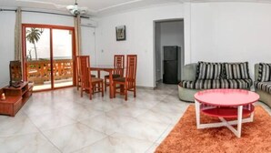 Un salon avec un canapé, une table à manger et des chaises, une table basse rouge et une plante en pot.