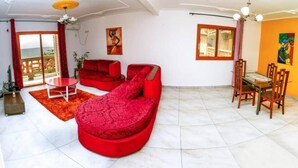 Un vaste espace de vie comprenant un canapé rouge, une table à manger avec des chaises et un balcon offrant une vue agréable.