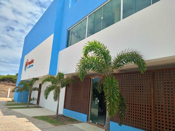 Un edificio con fachada azul y blanca, palmeras en primer plano y un letrero que dice "Hotel".