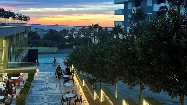 Ein Hotelinnenhof mit Außenbestuhlung, einem Pool und Blick auf den Sonnenuntergang.