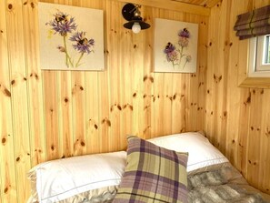 Une chambre de style cabane en bois, avec deux lits, une fenêtre ornée de rideaux à carreaux et des œuvres d’art florales accrochées aux murs.