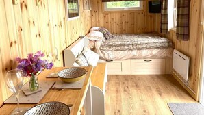A cozy wooden cabin room with a bed, a table with a vase of flowers, and a window with curtains. - Woodhead Shepherds Hut - Sleeps 2 - Parking (Perth)