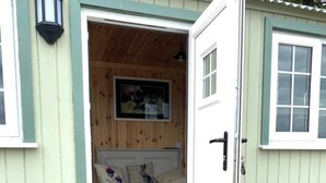 A wooden interior with a bench, a framed picture, and a door. - Woodhead Shepherds Hut - Sleeps 2 - Parking (Perth)