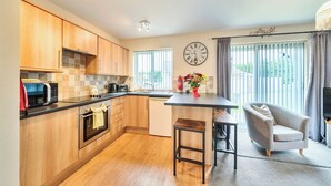 Una cocina moderna con armarios de madera, microondas, fregadero y comedor con una silla y mesa.