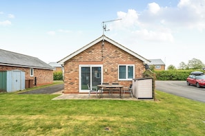 A brick house with a garage, a small patio with a table and chairs, and a red car parked on the street. - Cozy Dog Friendly cottage near Bridlington (Bridlington)