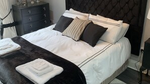 Une chambre à coucher moderne avec un grand lit, une tête de lit sombre, une table de chevet avec une lampe et un lustre.