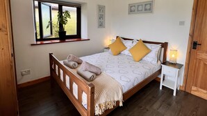 Een slaapkamer met een houten bed, een raam met een plant, een nachtkastje met een lamp en een deur.