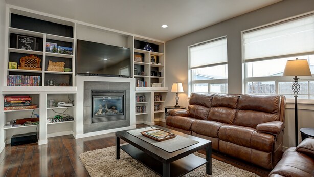 A living room with a fireplace, bookshelves, a brown leather sofa, and a flat-screen TV.