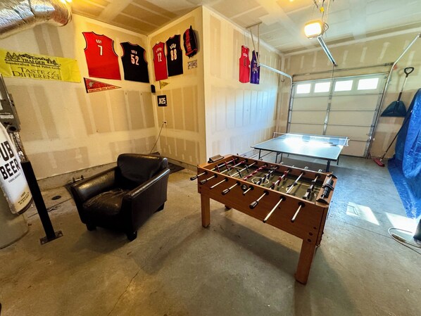 A garage with a foosball table, a black leather chair, and several sports jerseys on the wall. - Spacious, family getaway full of entertainment! (Redmond)