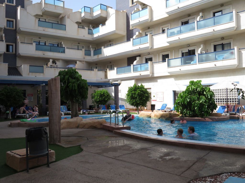 Un espace piscine doté de plusieurs niveaux de balcons, de chaises longues et où quelques personnes se baignent.