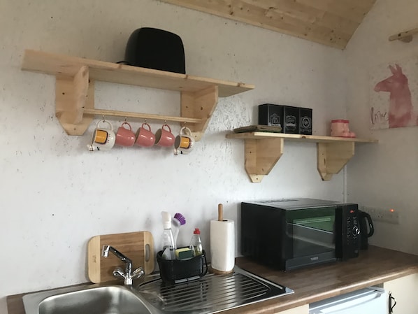 Eine Küche mit Holzböden, die Tassen und Kartons beherbergen, einer Mikrowelle und einem Spülbecken mit Schneidebrett.