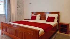 Een houten bed met rode en witte beddengoed, een nachtkastje en een klein houten kastje.
