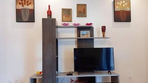 Een moderne woonkamer met een grijze entertainmentkast, een flatscreen televisie en decoratieve elementen zoals vazen en ingelijste foto's.
