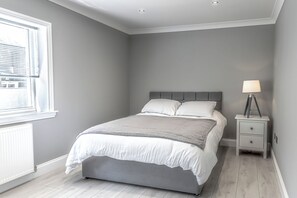 Une chambre à coucher avec un lit, une table de chevet, une lampe et une fenêtre.