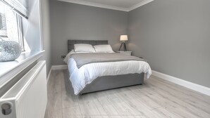 Et soveværelse med seng, sengebord, lampe og et vindue med persienner.