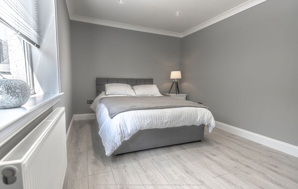 Une chambre à coucher avec un lit, une table de chevet, une lampe et une fenêtre avec des stores.