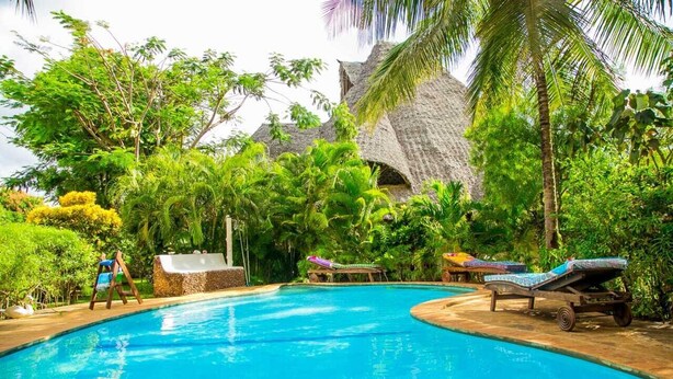 Une piscine entourée de chaises longues et agrémentée d’une structure au toit de chaume, le tout dans un cadre luxuriant et tropical.
