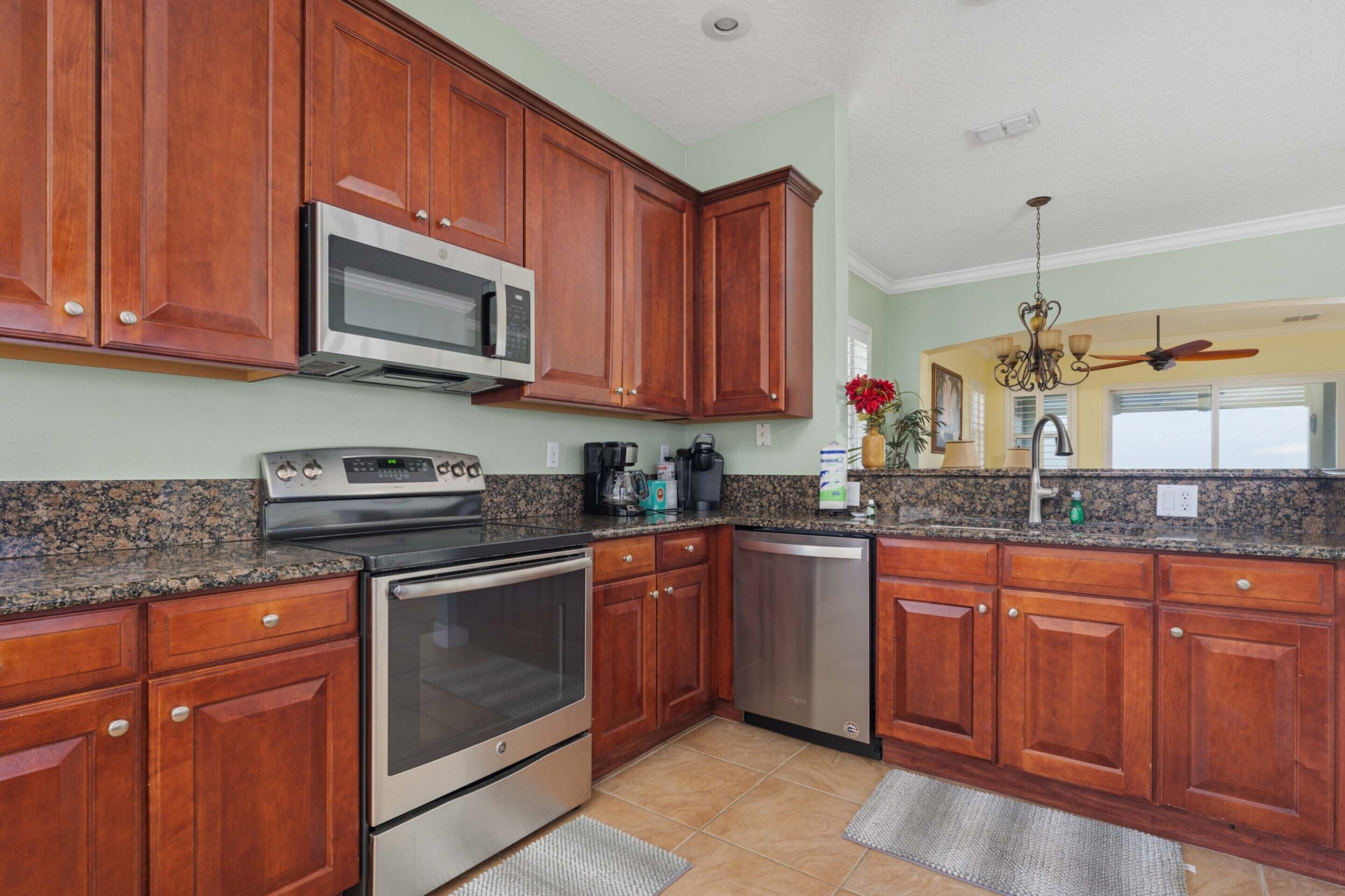A kitchen with wooden cabinets, stainless steel appliances, granite countertops, and a ceiling fan.