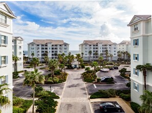 A multi-story hotel with a central courtyard, palm trees, and a view of the ocean.