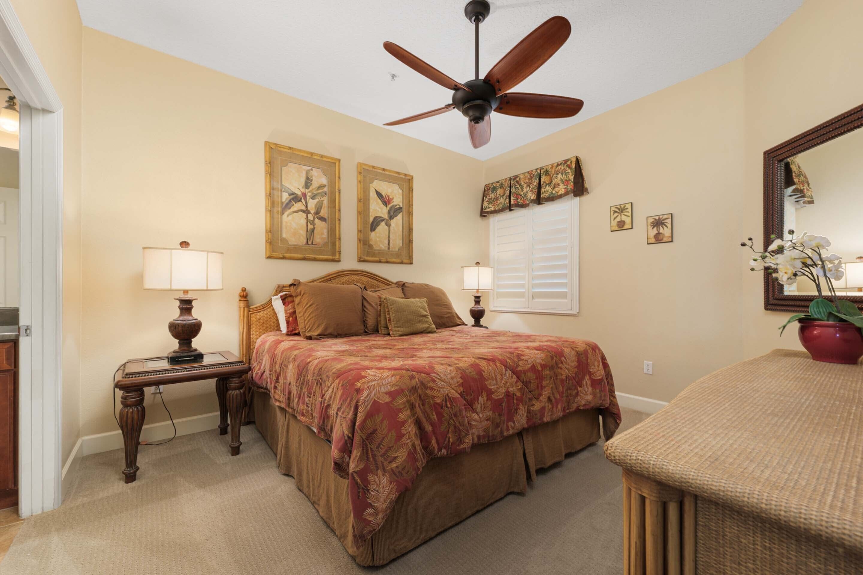 A bedroom with a bed, two bedside tables with lamps, a ceiling fan, and wall art.