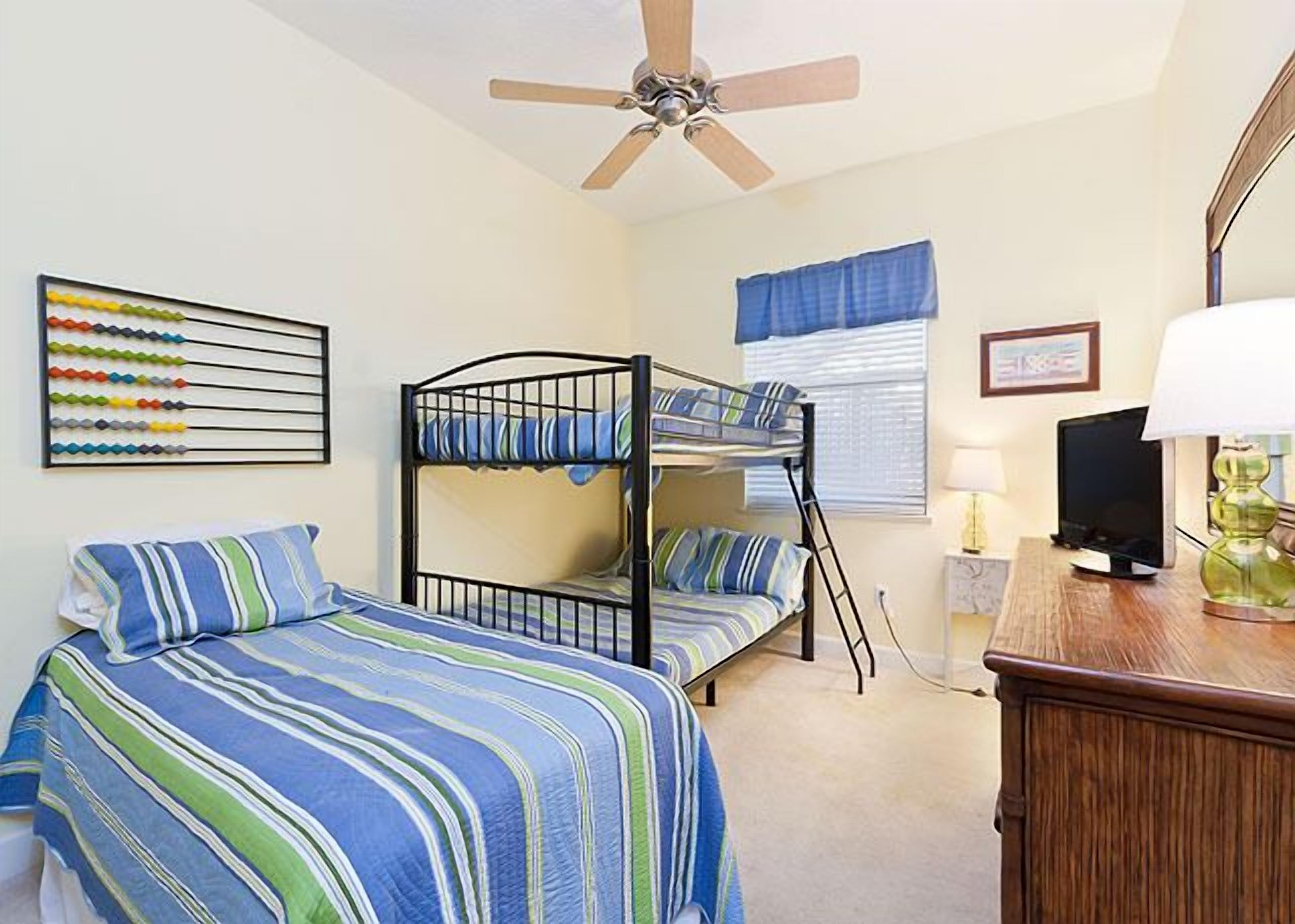 A room with bunk beds, a ceiling fan, a television, and a desk with a lamp.