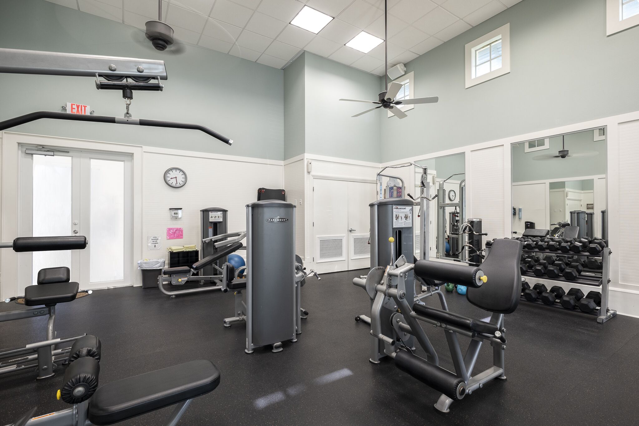 A gym with exercise equipment, a clock, and an exit sign.