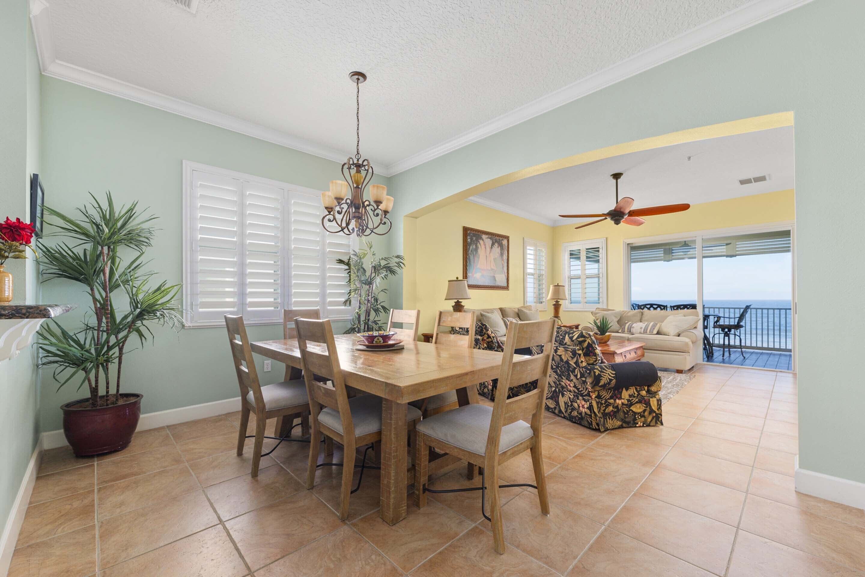 A dining area with a wooden table and chairs, a chandelier, and potted plants.