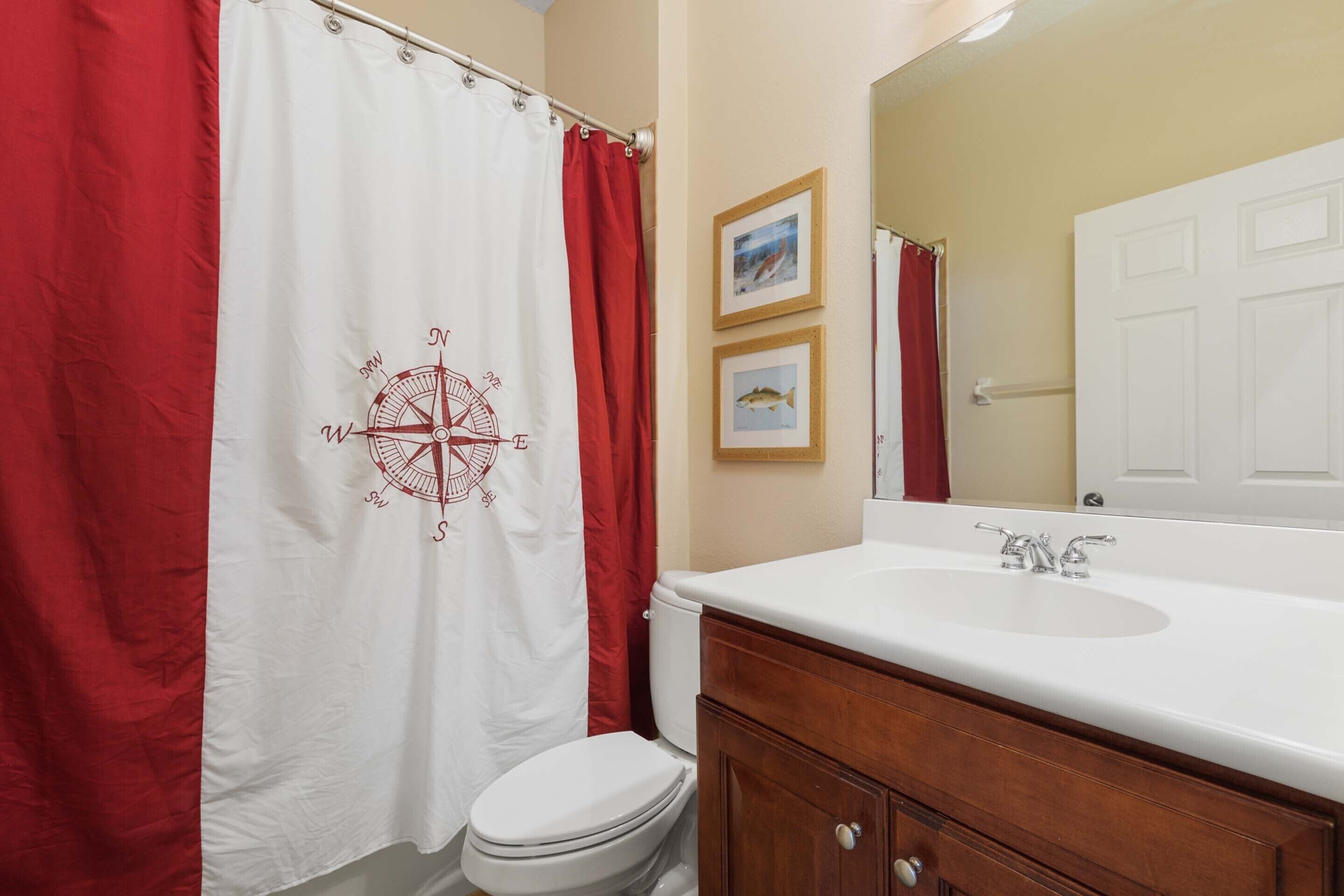 A bathroom with a white sink, wooden vanity, and a red and white shower curtain with a compass design.
