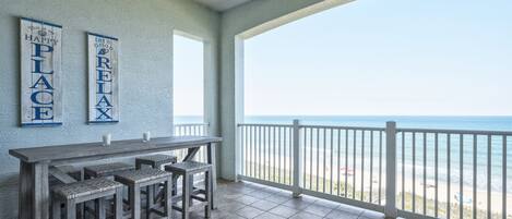 A balcony with a view of the beach, a wooden table with chairs, and two signs on the wall.