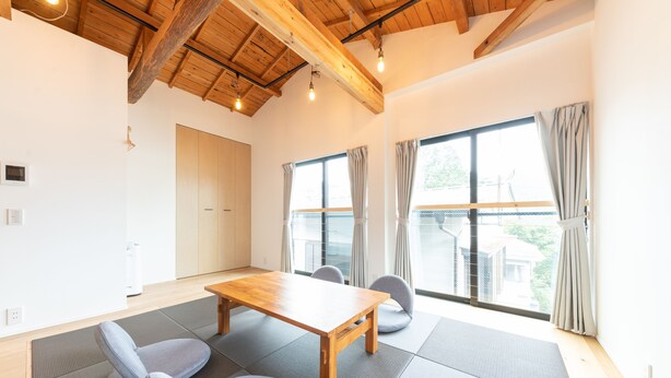 A spacious room with a wooden table and chairs, large windows with curtains, and a high ceiling with exposed beams. - Gora Base A (Hakone)