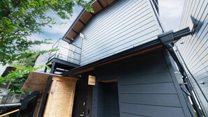 A modern building with a dark exterior, a wooden door, and a metal staircase leading to a balcony. - Gora Base A (Hakone)