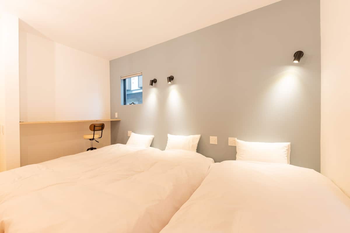 Habitación de hotel con dos camas, un ventanal pequeño e iluminación instalada en la pared.