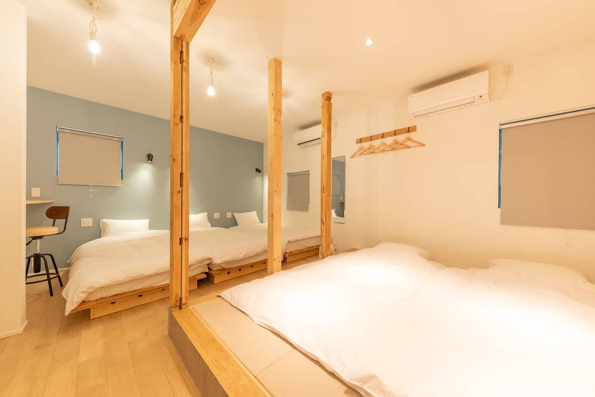 Una habitación con tres camas de madera, un escritorio con una silla y un aire acondicionado instalado en la pared.