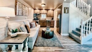 Una sala de estar acogedora con sofá, mesa de centro y una escalera que lleva a una zona de cocina.