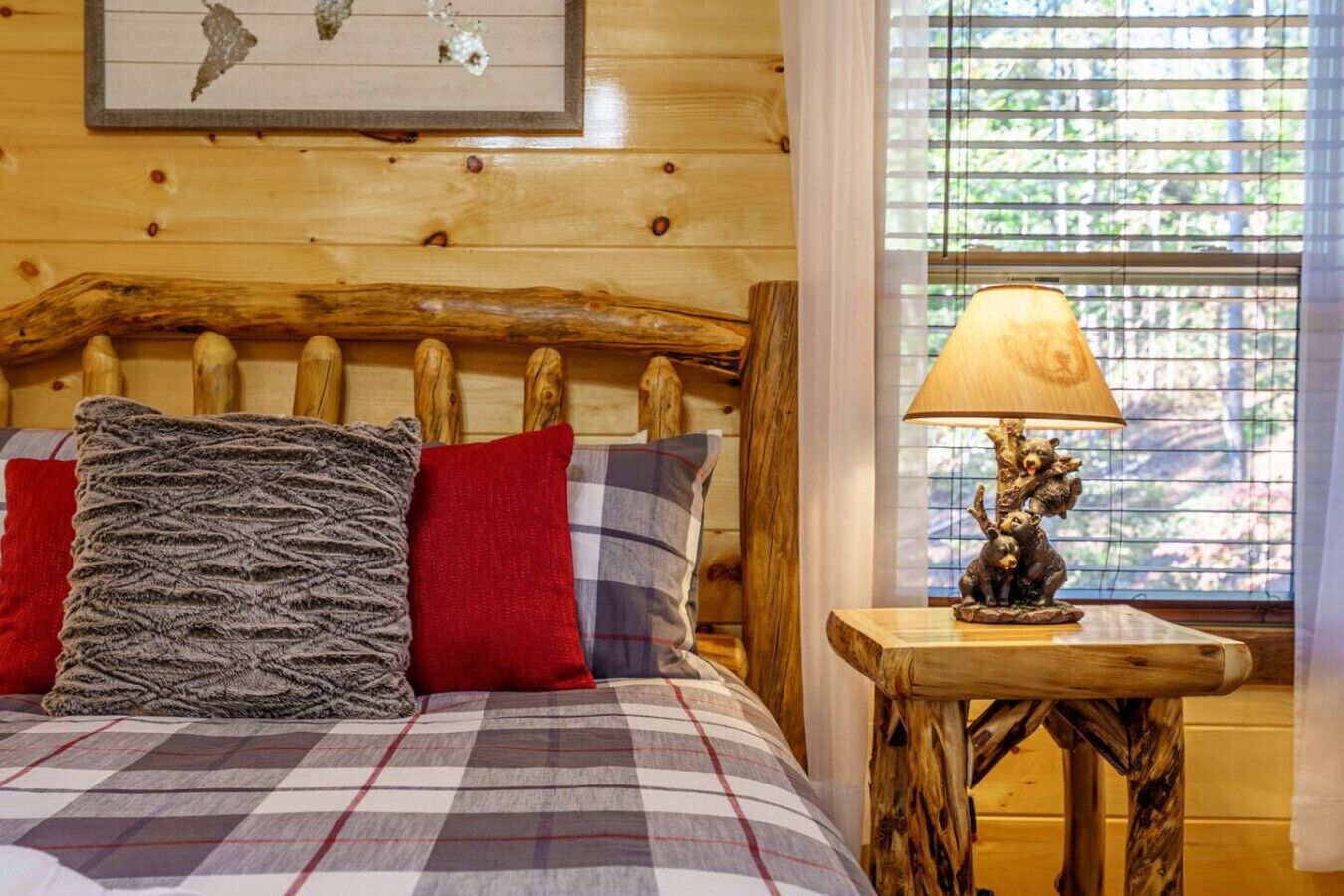A cozy wooden cabin room with a bed, pillows, a lamp, and a window with blinds.