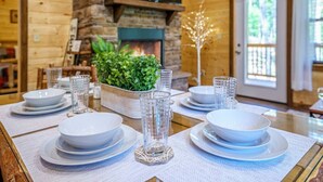 A dining table set with white plates and clear glasses, a potted plant, and a decorative tree in a room with wooden walls and a stone fireplace. - Great Location! Pigeon Forge, Pool Table/Hot Tub & Game Room, Quiet Neighborhood (Sevierville)
