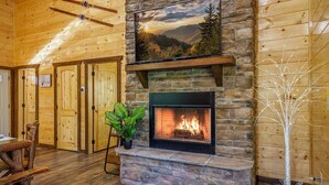 A cozy room with a stone fireplace, wooden walls, and a view of the mountains. - Great Location! Pigeon Forge, Pool Table/Hot Tub & Game Room, Quiet Neighborhood (Sevierville)