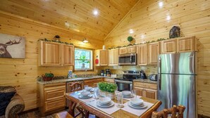 A wooden cabin kitchen with wooden cabinets, a stainless steel refrigerator, and a dining table set for four. - Great Location! Pigeon Forge, Pool Table/Hot Tub & Game Room, Quiet Neighborhood (Sevierville)