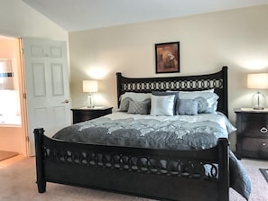 A bedroom with a large bed, two bedside tables with lamps, a door, and a framed picture on the wall.