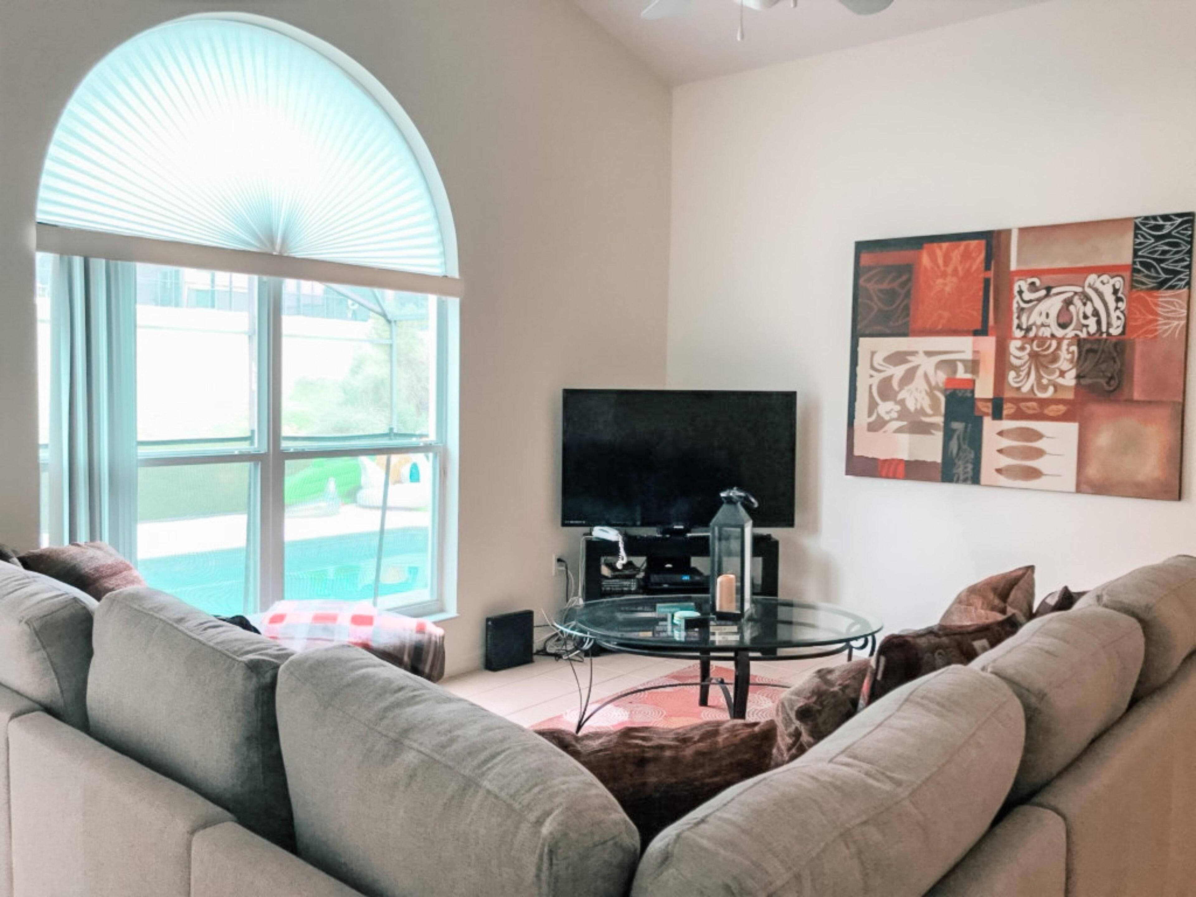 A living room with a large window, a flat-screen TV, a glass coffee table, and a modern abstract painting on the wall.