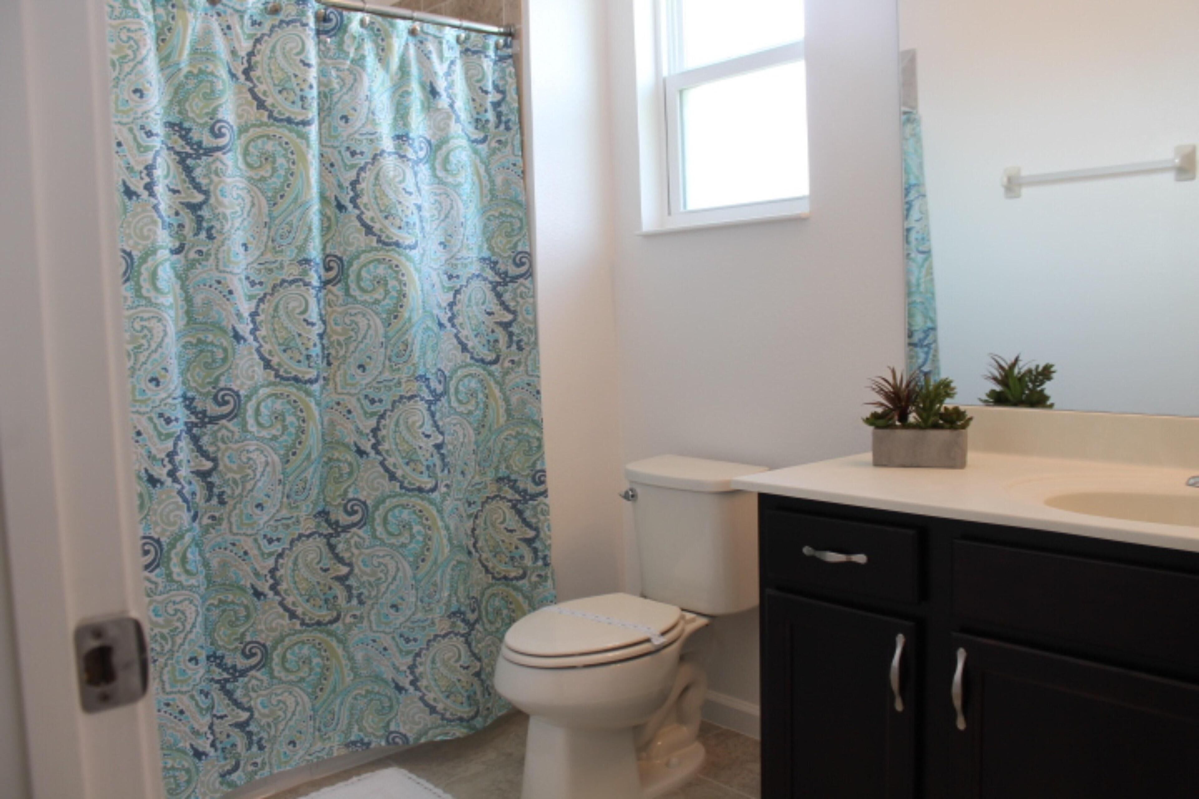 A bathroom with a toilet, a sink, a mirror, and a shower curtain.