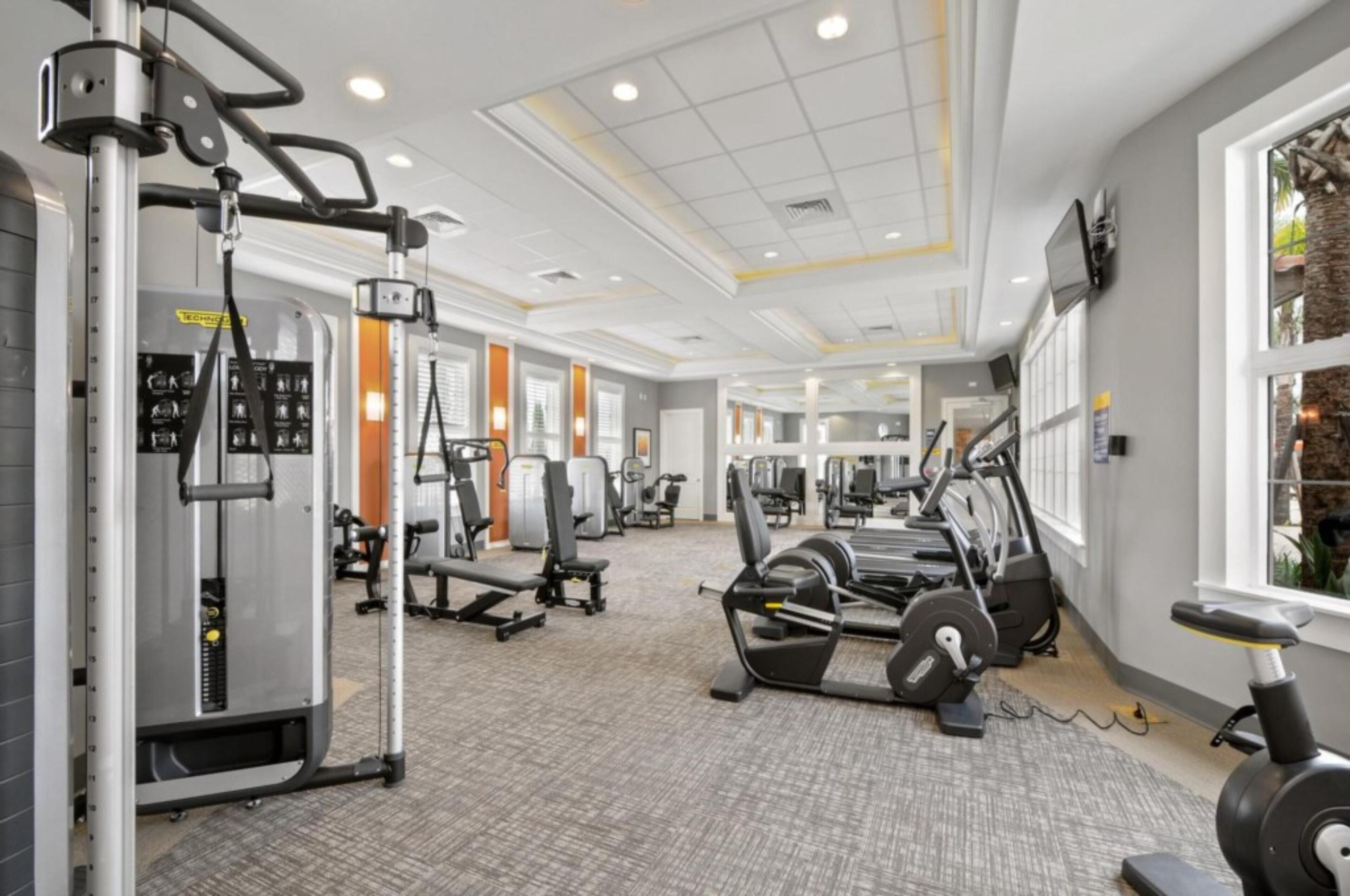A gym with various exercise machines, a large window, and a ceiling with recessed lighting.
